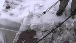 Person clearing snow from a roof edge with a roof rake to prevent ice dams